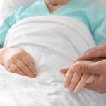 elderly person in hospital holding hands with caregiver