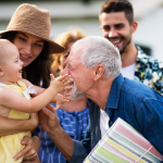 Woman with hat holding young baby that is grabbing grandpas face while dad watches on