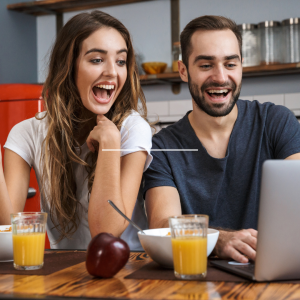Young adult female and male eating breakfast while looking at lap top screen