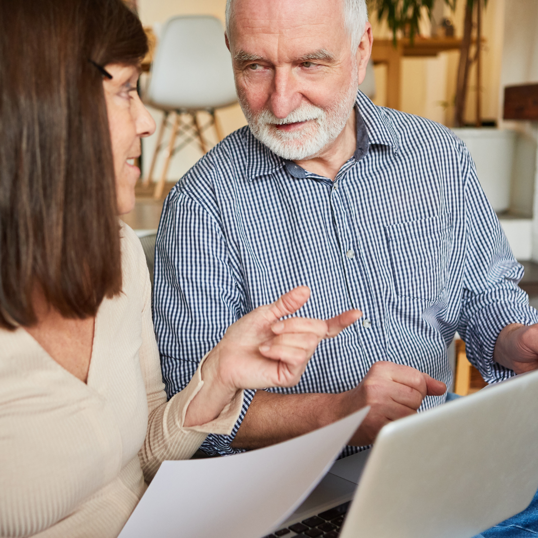 Woman holding paper with older man in front of a laptop screen